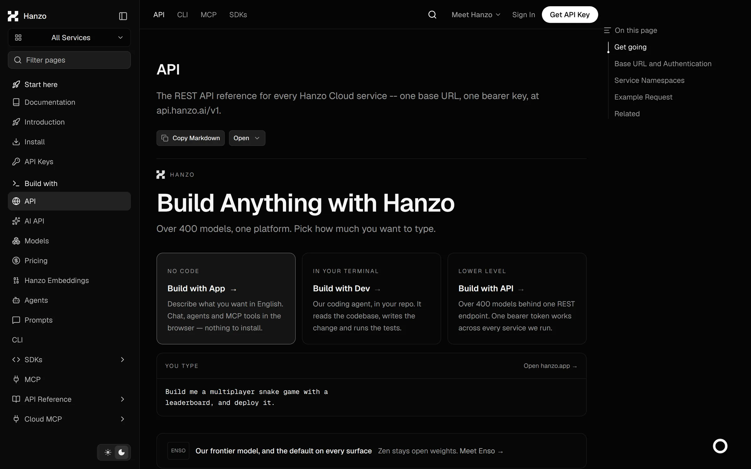 Hanzo API reference page in dark mode: a left sidebar with an All Services picker, a page filter and nav entries for Start here, Introduction, Install, API Keys, API, AI API, Models, Pricing, Embeddings, Agents, Prompts, SDKs, MCP and API Reference; the main column headed "API" describes one base URL and one bearer key at api.hanzo.ai/v1 with Copy Markdown and Open controls, followed by "Build Anything with Hanzo" and three route cards — Build with App, Build with Dev and Build with API; an on-this-page rail sits at the right.